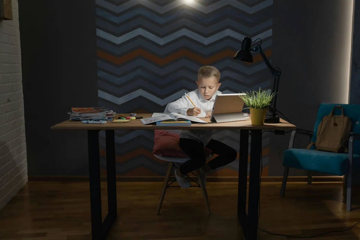 Young boy focused on homeschool homework at desk with books and tablet