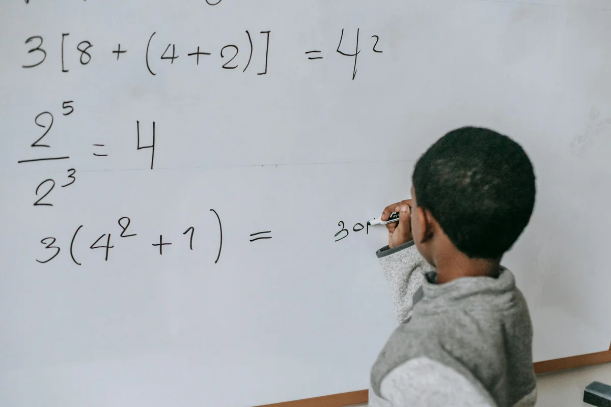 Focused child solving math equations on whiteboard during homeschool lesson