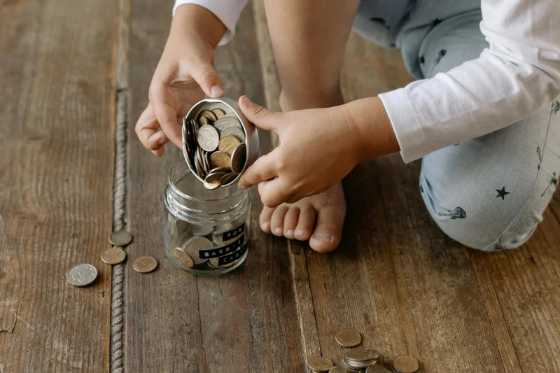 Child adding coins to savings jar - homeschool budget planning and savings strategies