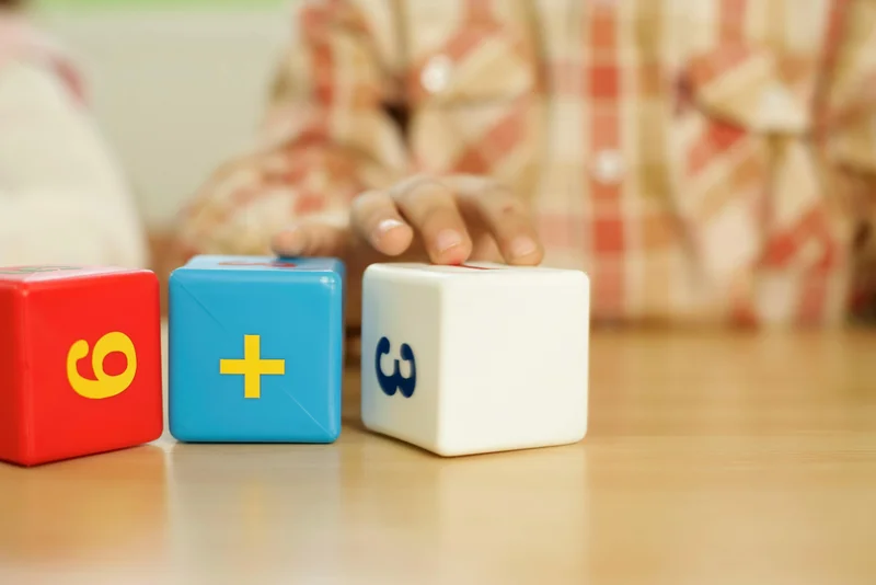 Child's hand touching colorful educational math blocks on desk - hands-on learning with Horizons Math curriculum