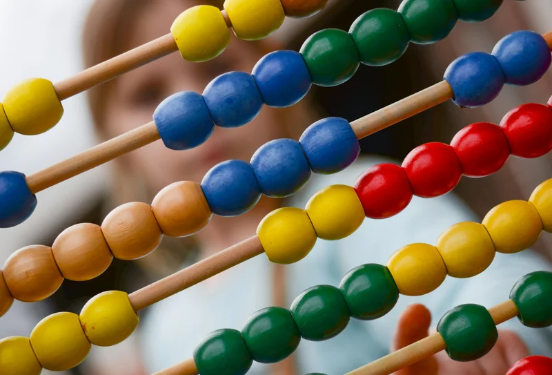 Child using colorful abacus beads for math learning - spiral approach builds skills through repeated practice